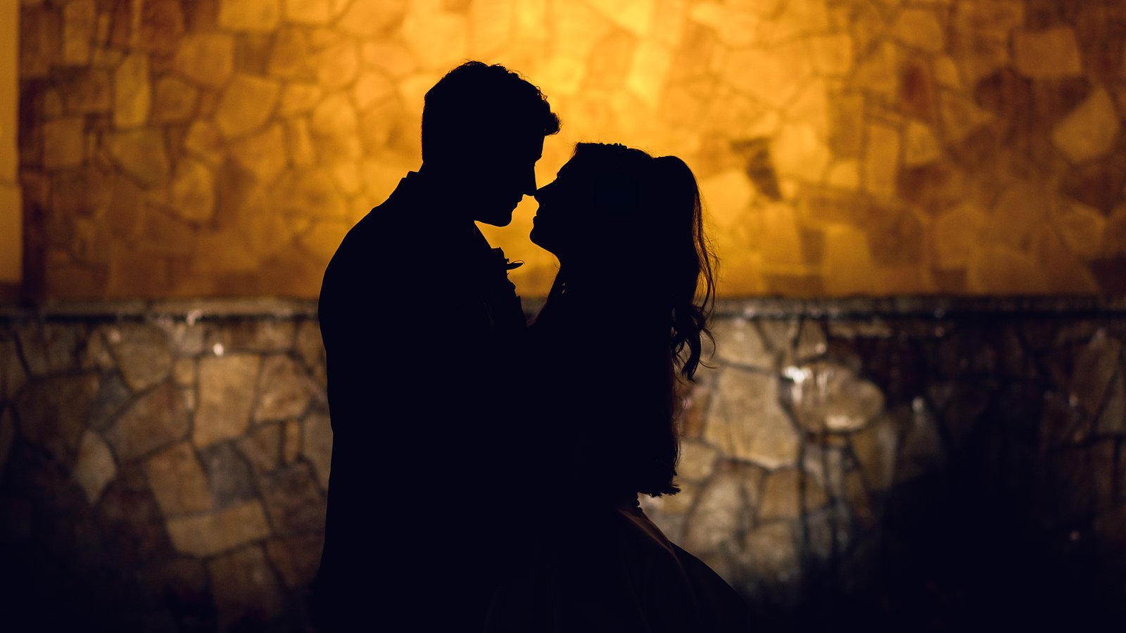Casey and Matthew leaning together in silhouette against a glowing golden stone wall